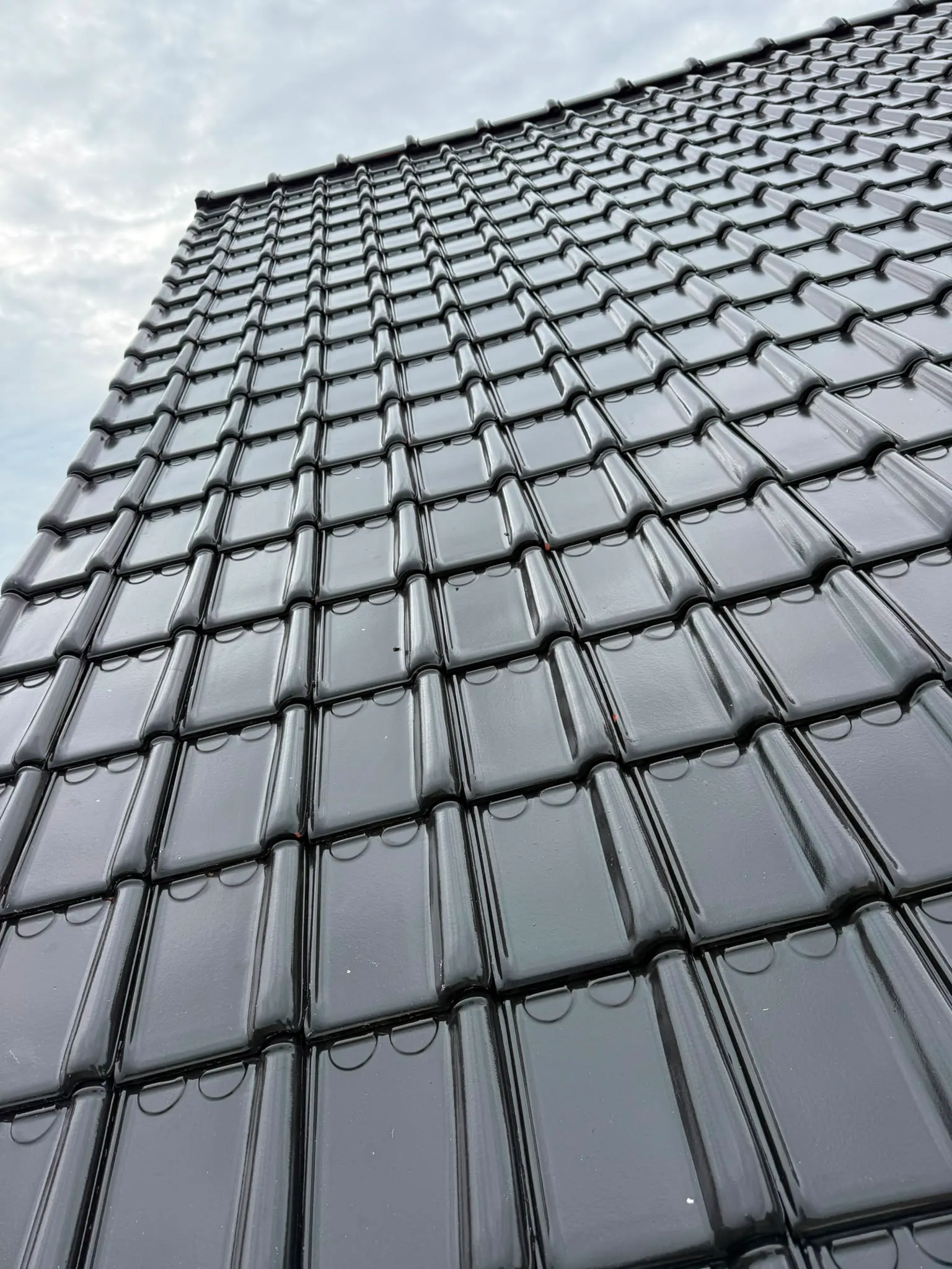 Vue en contre-plongée d’un pan de toiture en tuiles noires brillantes, Namur