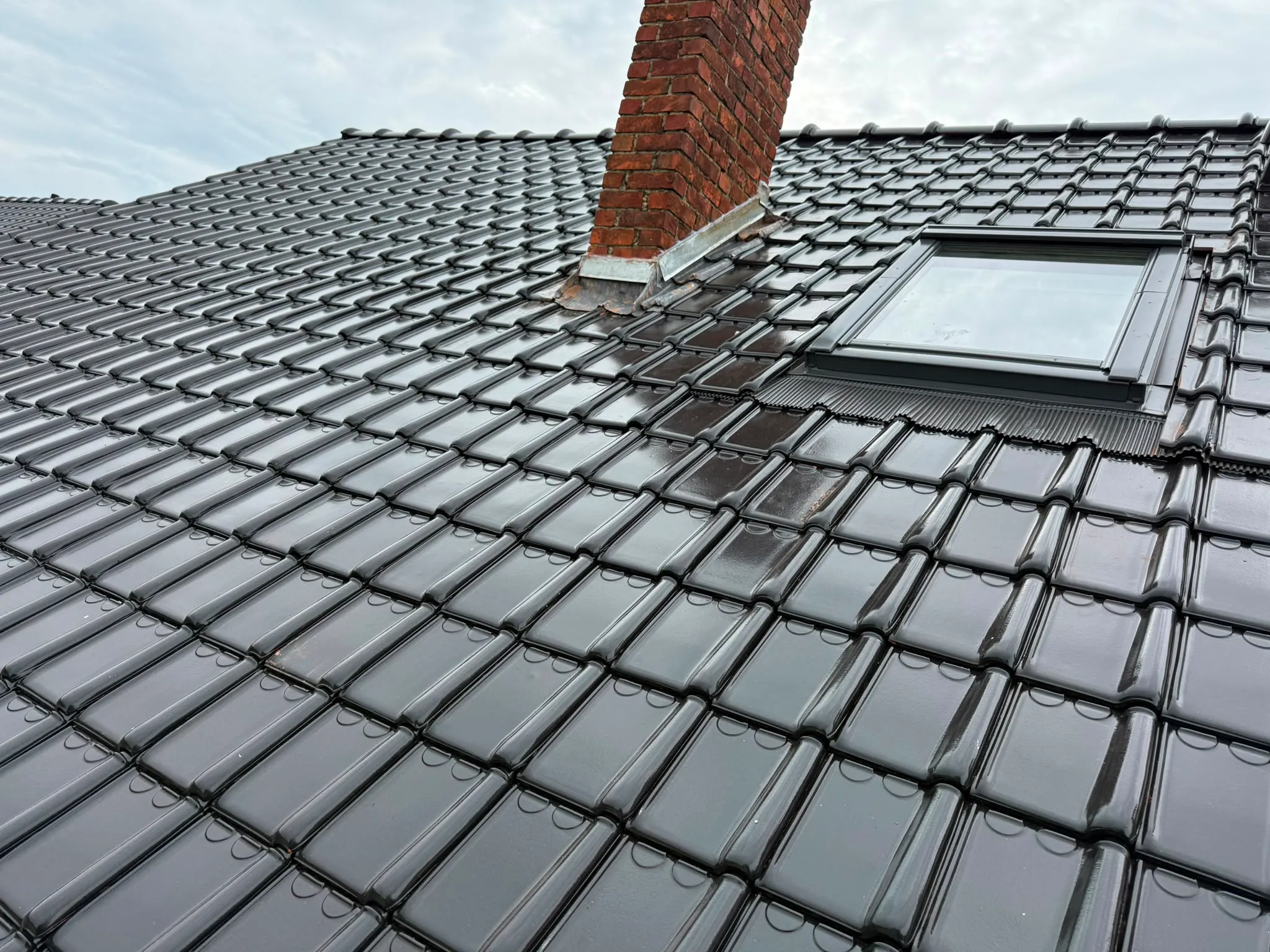 Fenêtre de toit fraîchement posée dans une toiture en tuiles noires, près d’une cheminée à solin zinc, Namur