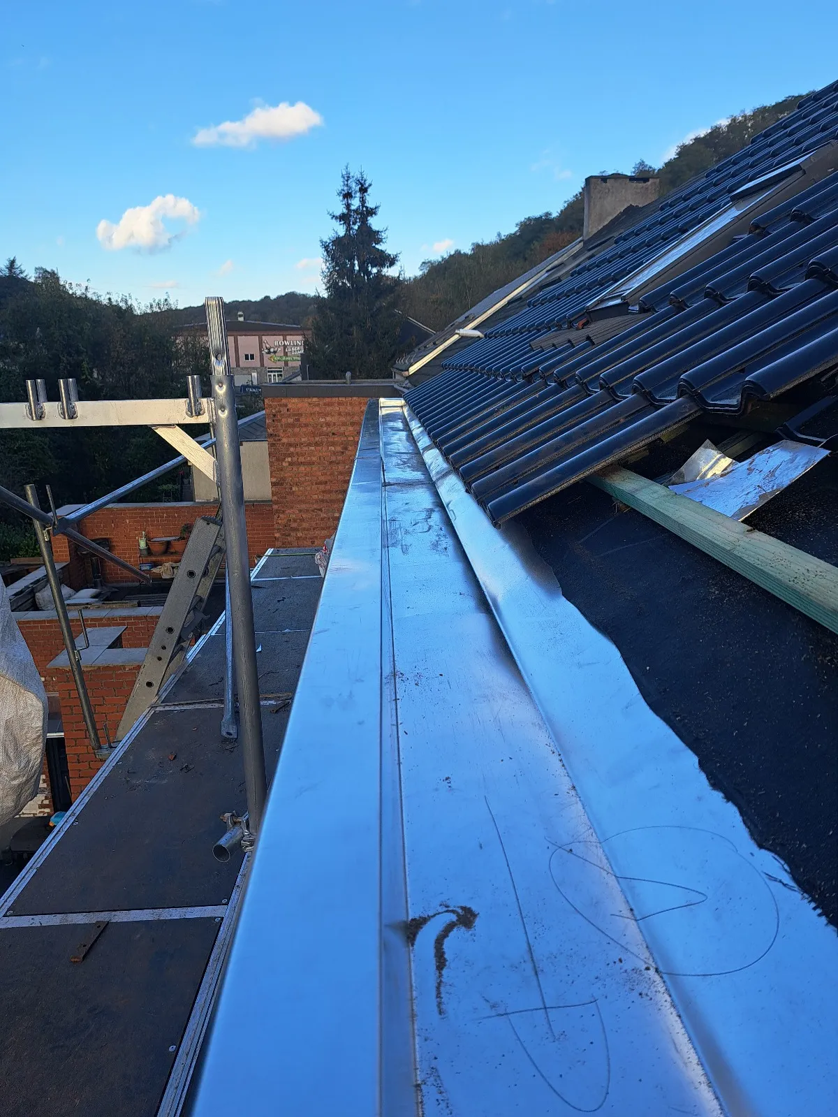 Chéneau en zinc longeant une toiture en tuiles noires avec cheminée en briques et échafaudage, Jambes