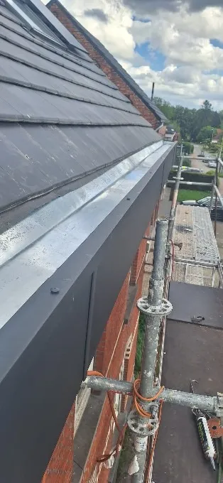 Chéneau en zinc neuf longeant un pan de toiture en ardoises, échafaudage en place, Charleroi