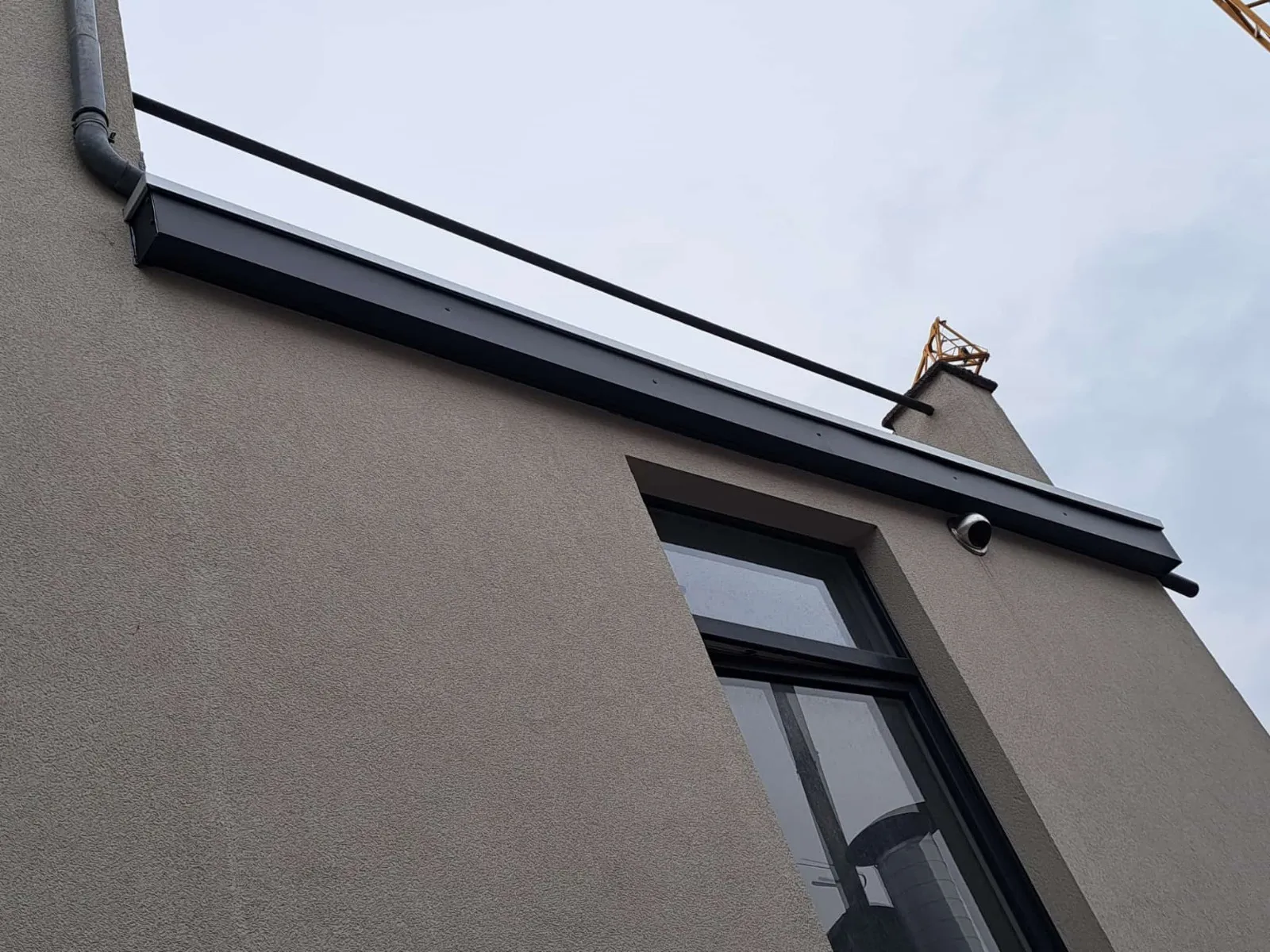 Corniche et gouttière en zinc le long d’un pignon crépi, vue en contre-plongée, Namur