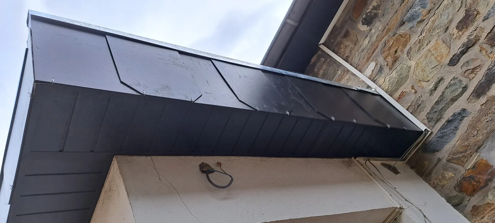 Débord de toit habillé de tôle laquée anthracite contre une façade en pierres apparentes, Dinant