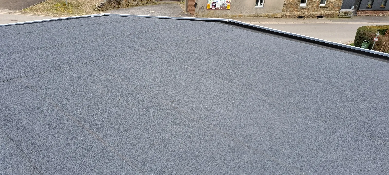 Toiture plate neuve en membrane d’étanchéité avec relevés en zinc, surplombant un village