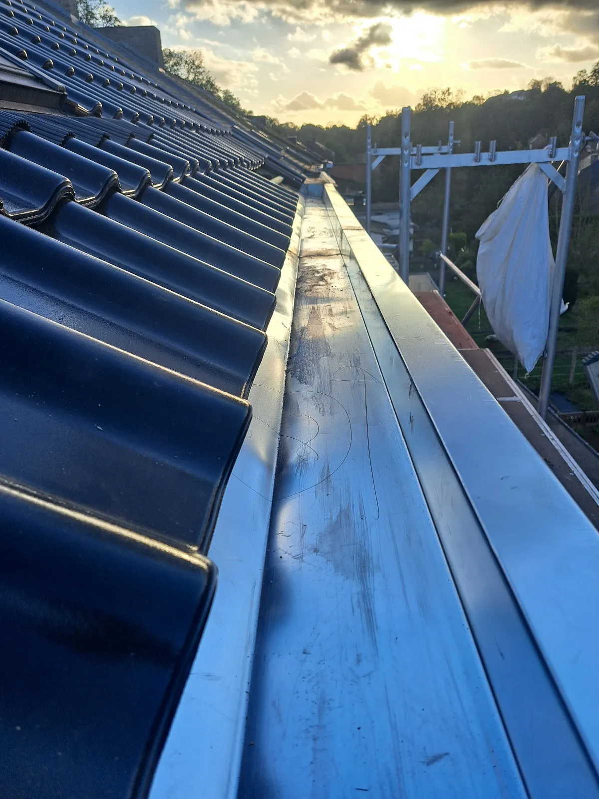 Chéneau en zinc neuf le long d’une toiture en tuiles noires au coucher du soleil